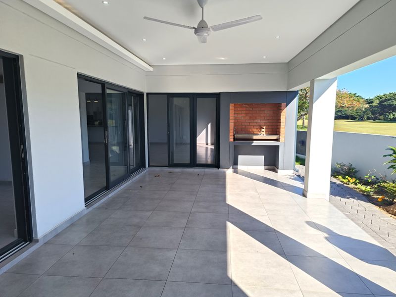 A spacious covered patio featuring tiled flooring, a built-in brick braai, and recessed lighting, offering seamless indoor-outdoor flow through large sliding glass doors.