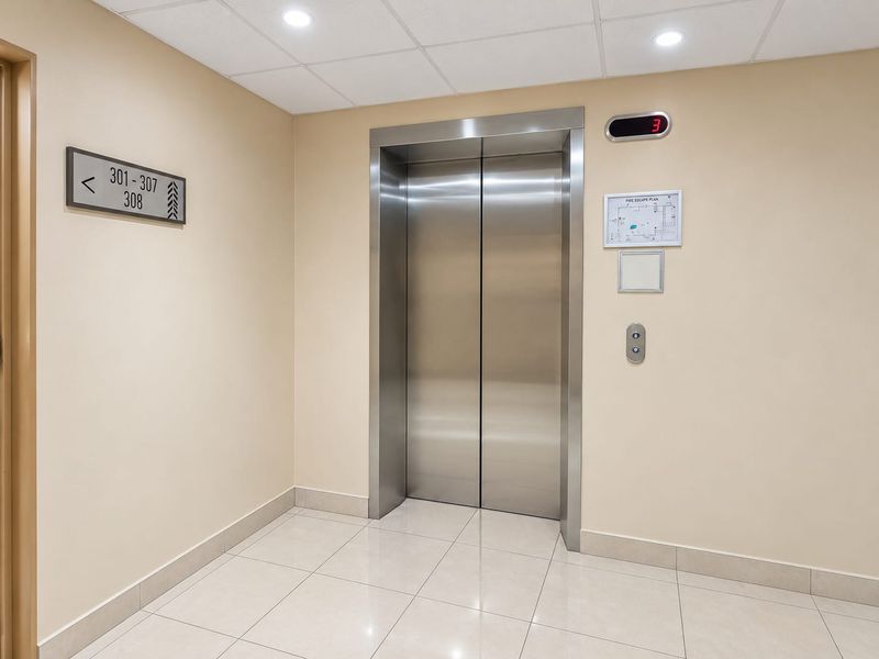 A clean and well-maintained apartment building elevator lobby featuring stainless steel elevator doors, tiled flooring, and recessed lighting.