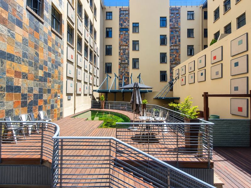 A communal outdoor pool area featuring timber decking, metal safety railings, and decorative stone-clad building facades within an apartment complex courtyard.