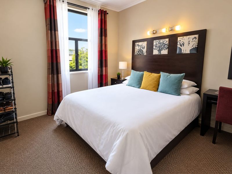A well-maintained bedroom featuring neutral wall tones, carpeted flooring, and a built-in headboard with integrated lighting.