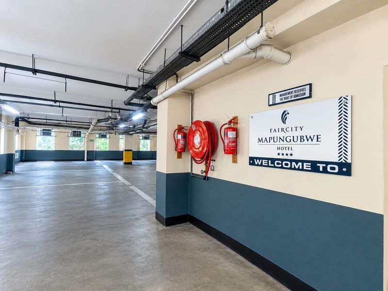 A clean, well-maintained underground parking garage featuring exposed ceiling infrastructure, fire safety equipment, and clear floor markings.