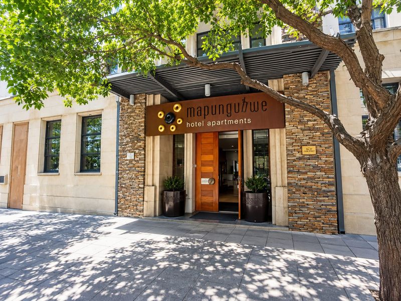 The main entrance of Mapungubwe Hotel Apartments, featuring a modern timber door, stone-clad facade, and a sleek metal awning.