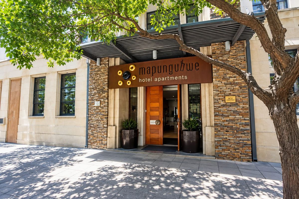 The main entrance of Mapungubwe Hotel Apartments, featuring a modern timber door, stone-clad facade, and a sleek metal awning.