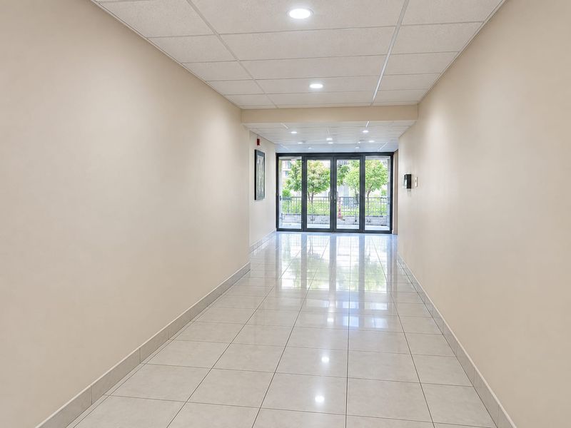 A bright and spacious hallway featuring polished tiled flooring, recessed ceiling lighting, and glass sliding doors leading to an outdoor area.
