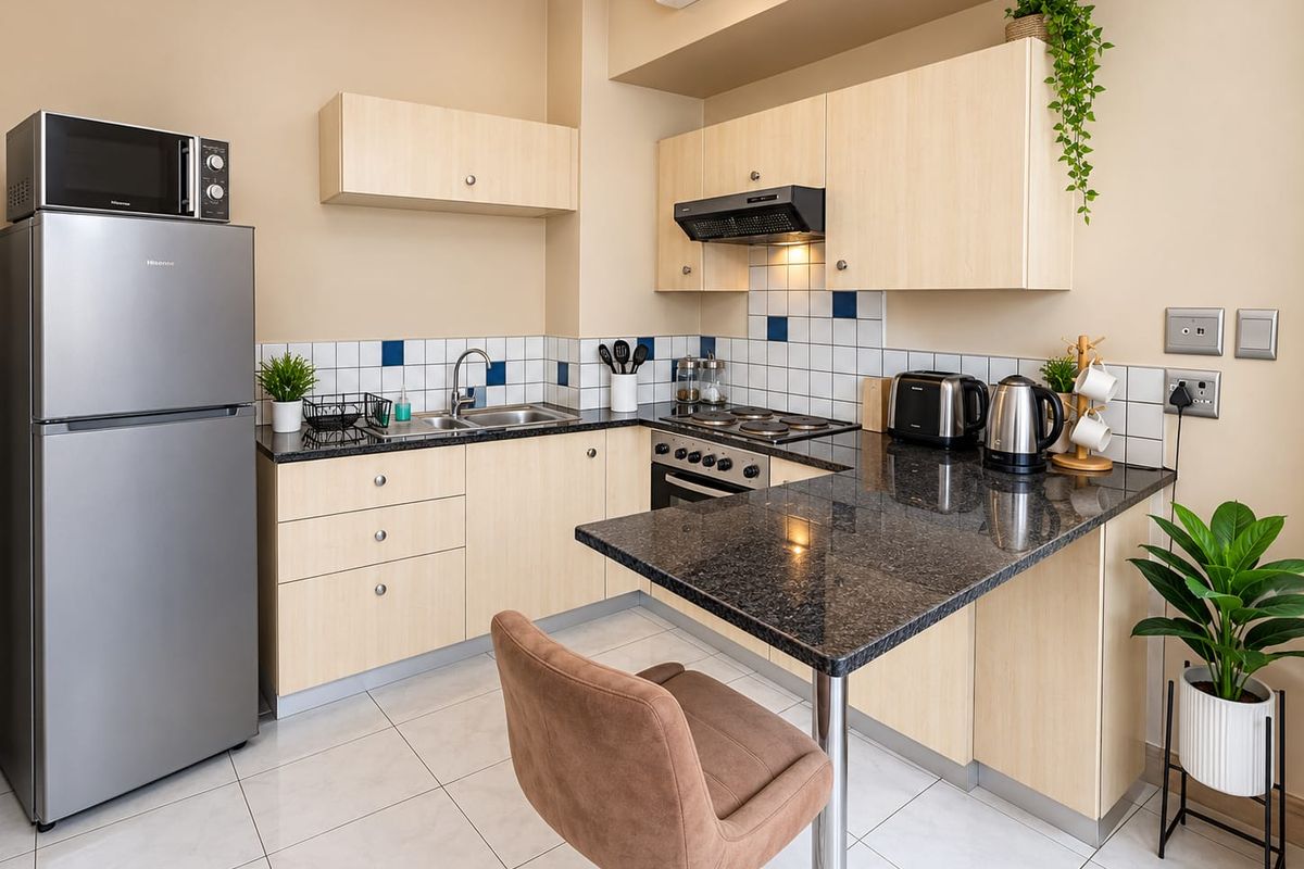 A well-maintained kitchen featuring light wood cabinetry, granite countertops, a breakfast bar, and integrated appliances, finished with modern tiled backsplash and flooring.