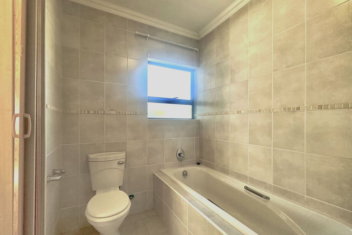 A functional bathroom featuring a built-in bathtub, toilet, and neutral ceramic tiling throughout, offering a clean and simple layout.