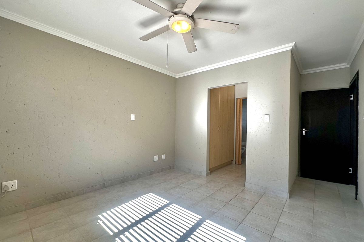 An empty bedroom featuring tiled flooring, a ceiling fan, and built-in cupboards, with direct access to an adjoining space.