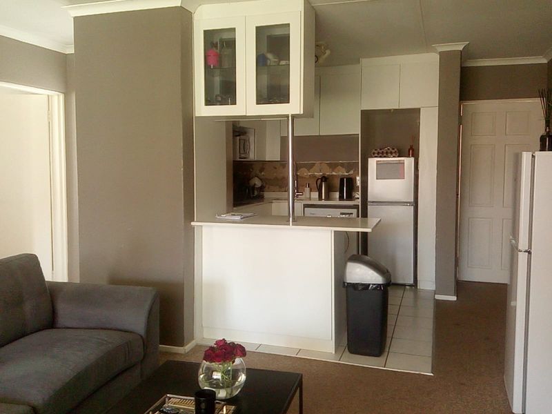 Open plan living area featuring a compact kitchen with breakfast bar, white cabinetry, and tiled flooring, providing a functional layout for modern apartment living.