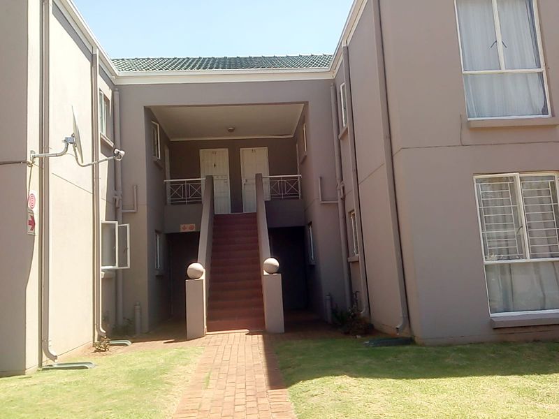 Exterior view of an apartment complex featuring a central staircase leading to upper-level units, paved walkway, and established lawn area.