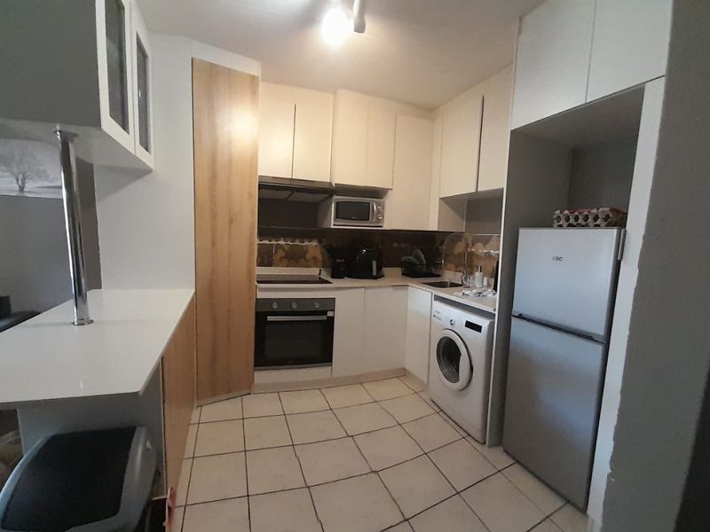 Compact kitchen featuring white cabinetry, built-in oven and hob, tiled flooring, and a breakfast bar, offering a functional layout for apartment living.