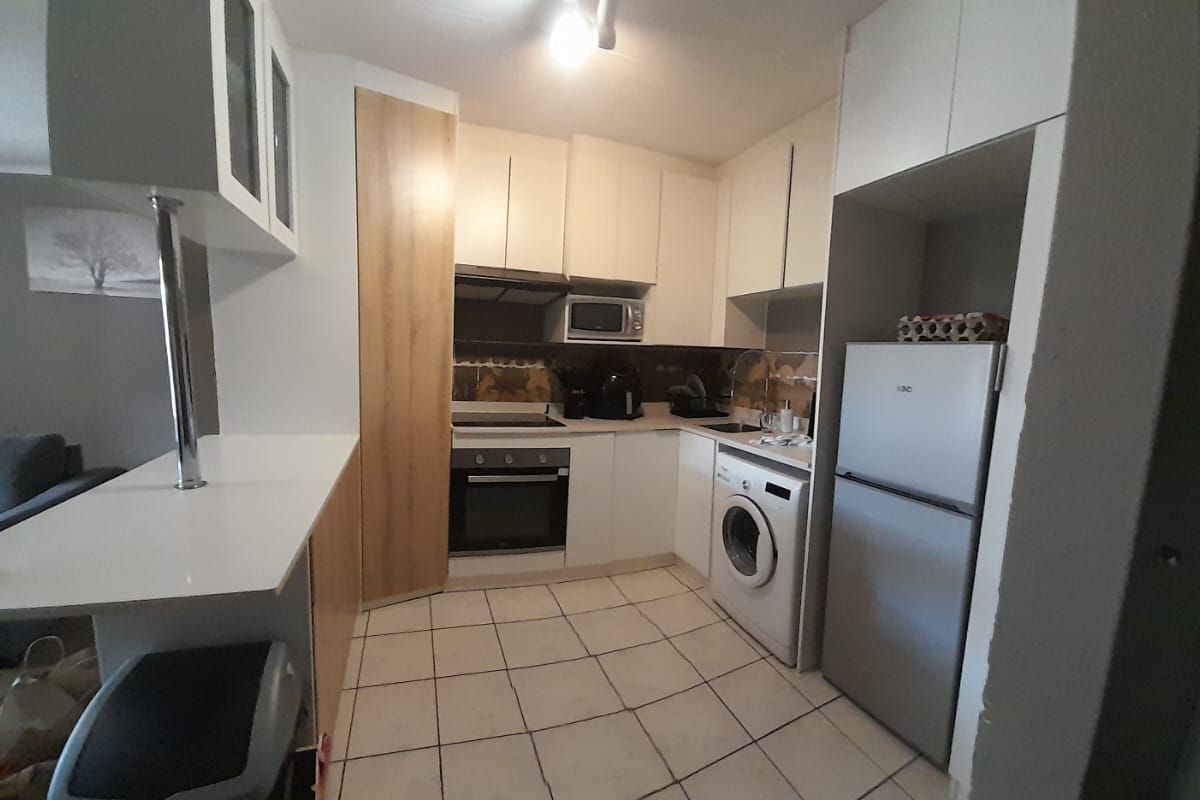 Compact kitchen featuring white cabinetry, built-in oven and hob, tiled flooring, and a breakfast bar, offering a functional layout for apartment living.