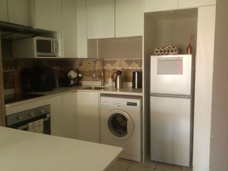 Compact kitchen featuring white cabinetry, built-in appliances, and a washing machine, currently requiring repair to the tiled splashback area.