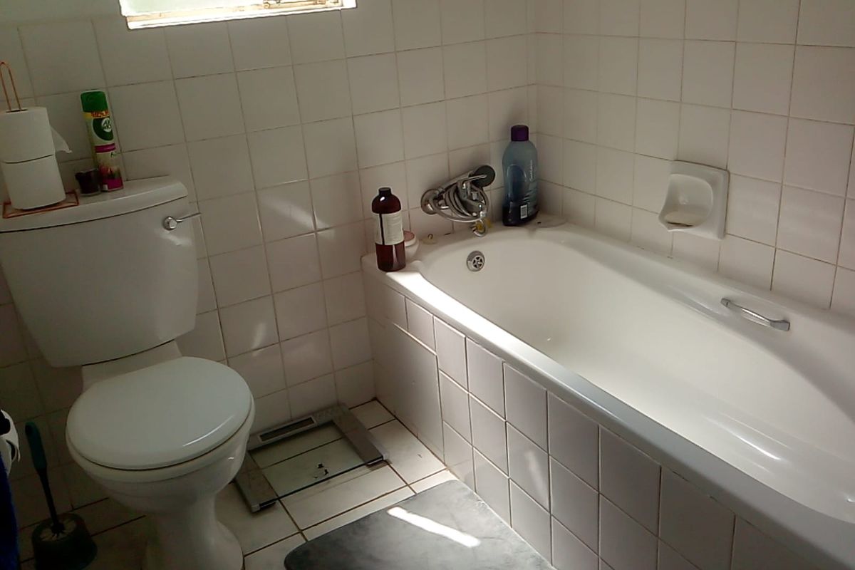 A functional bathroom featuring a built-in bathtub, white ceramic wall tiling, and a standard toilet suite.