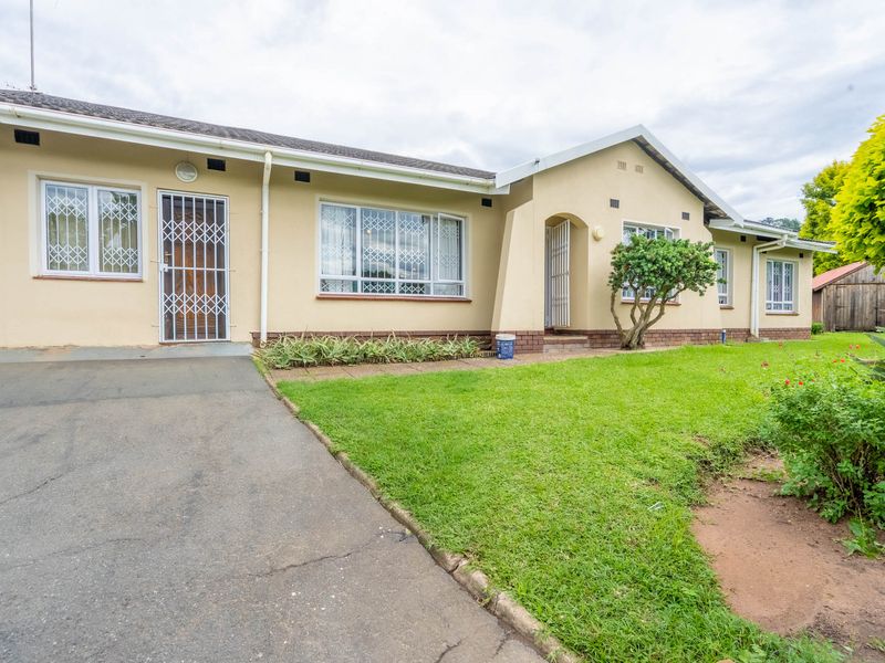 Front elevation of a single-story house featuring a paved driveway, security gates, and established garden area.