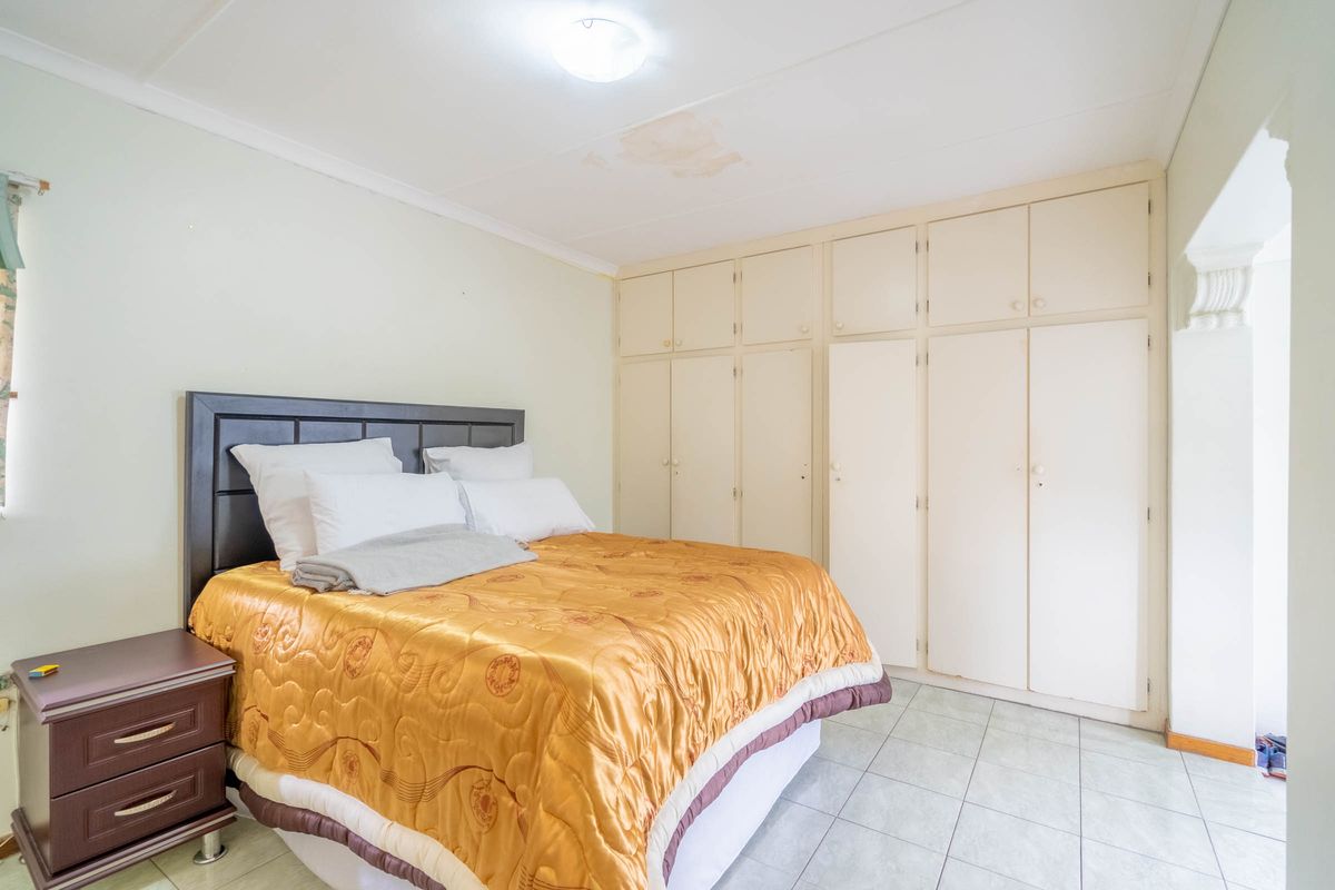A bedroom featuring built-in cupboards, tiled flooring, and visible water staining on the ceiling.
