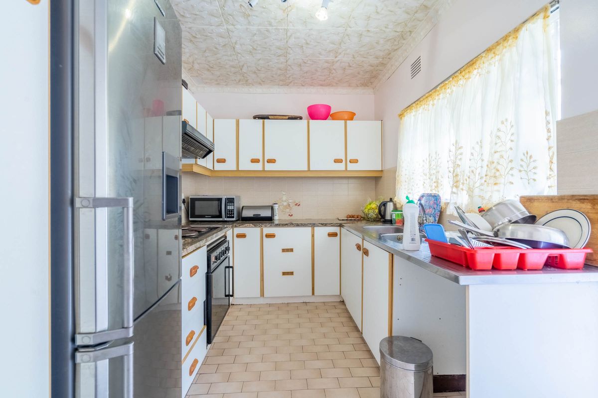 A functional kitchen featuring white cabinetry, laminate countertops, a built-in oven with extractor fan, and tiled flooring, offering potential for modern updates.