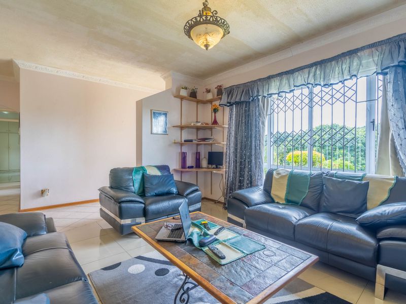 A living room featuring tiled floors, decorative ceiling cornices, and a large window with security bars, offering a functional space with potential for modernization.