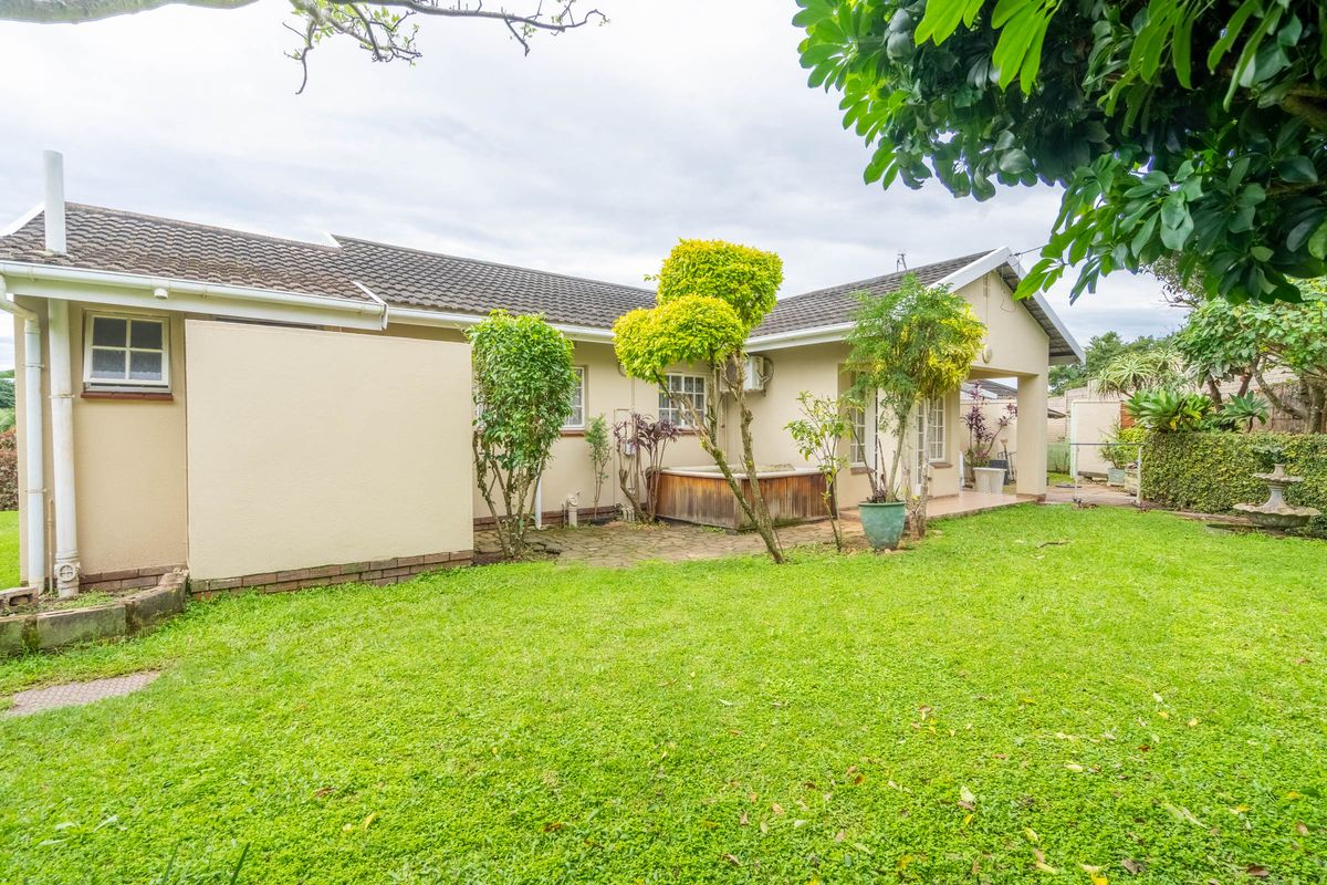 A view of the rear exterior of the house featuring a paved patio area, well-maintained lawn, and established garden landscaping.
