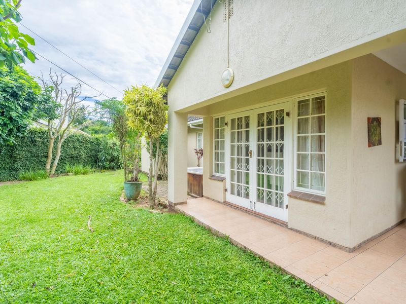 A covered patio area featuring tiled flooring and french doors leading into the home, overlooking a private garden space.
