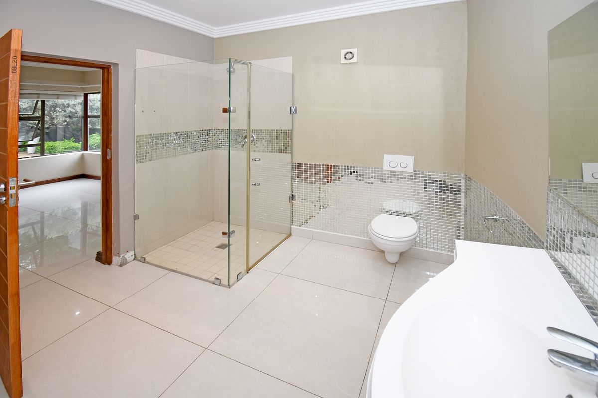 A modern bathroom featuring a glass-enclosed walk-in shower, wall-mounted toilet, and vanity basin with neutral floor tiling.
