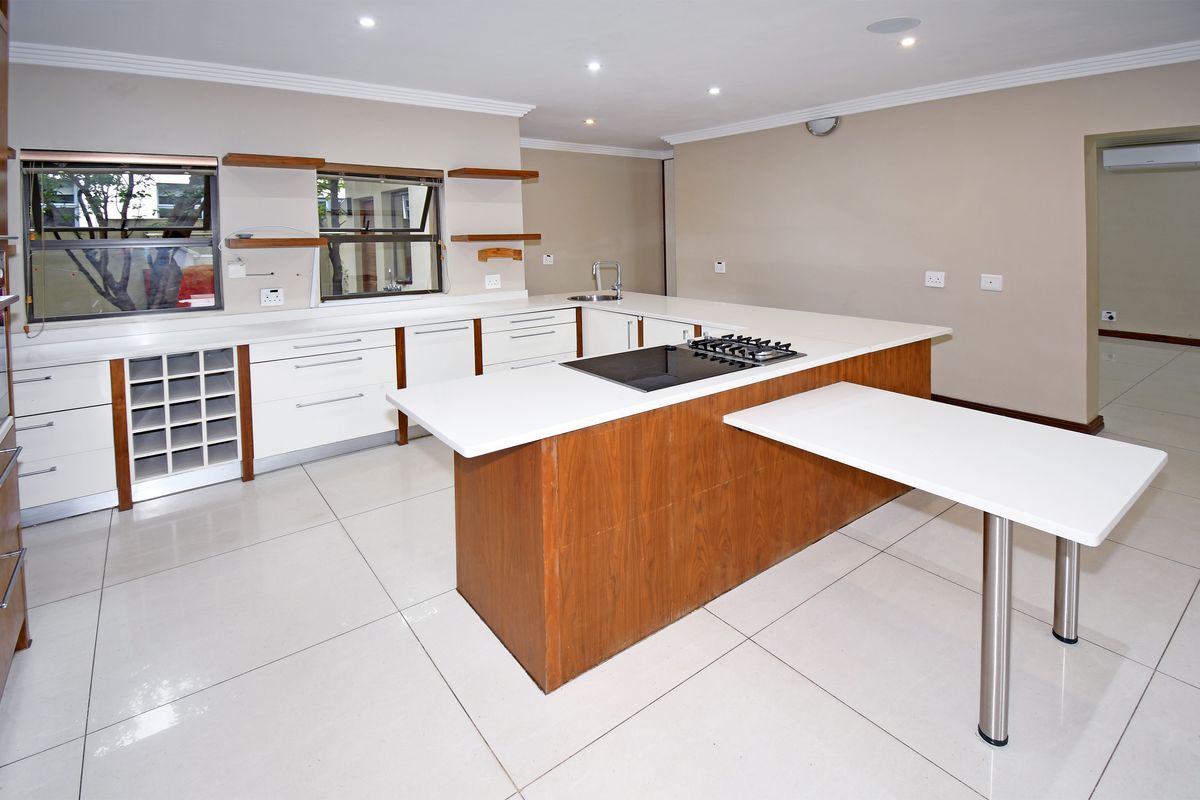 Modern open-plan kitchen featuring white cabinetry, stone countertops, a central island with a built-in gas hob, and tiled flooring throughout.