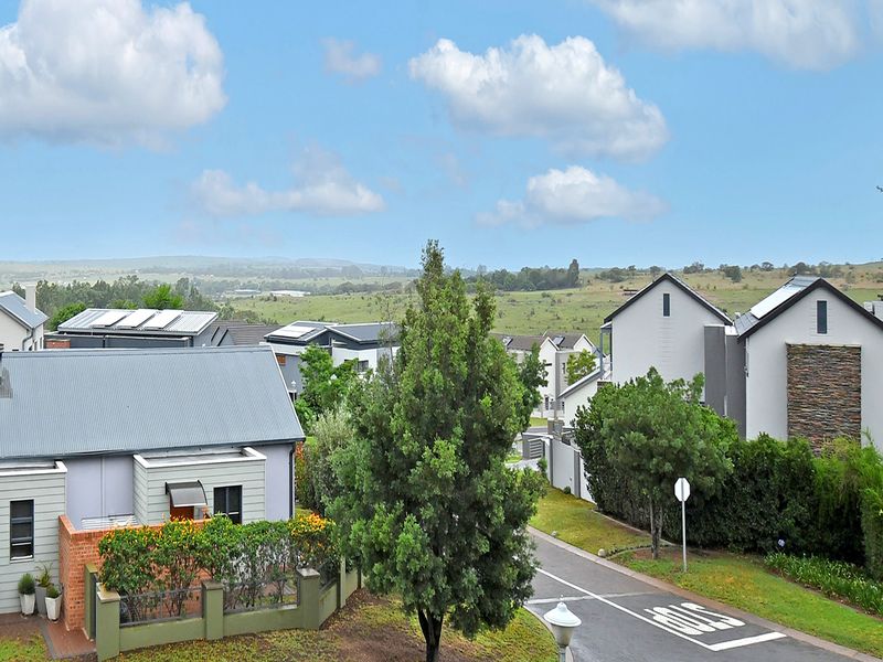 An elevated view overlooking a modern residential estate with well-maintained homes, paved streets, and expansive green landscape surroundings.