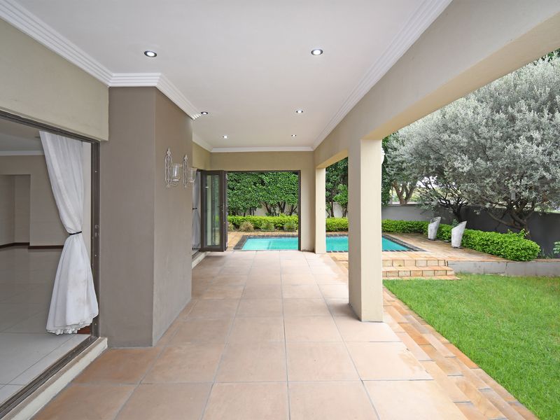 A spacious covered patio featuring tiled flooring and recessed lighting, providing seamless indoor-outdoor flow to the swimming pool and landscaped garden area.