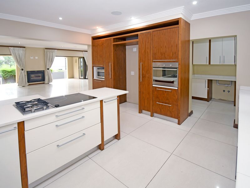 Modern open-plan kitchen featuring a central island with a built-in hob, integrated oven, and a separate scullery area with ample cabinetry.