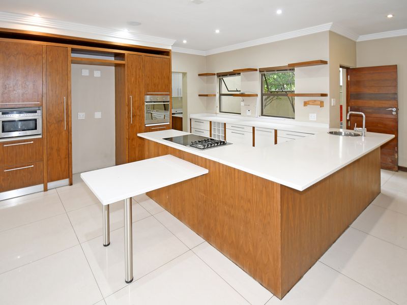 Modern kitchen featuring wood-veneer cabinetry, white stone countertops, a central island with a built-in hob, and integrated oven and microwave.