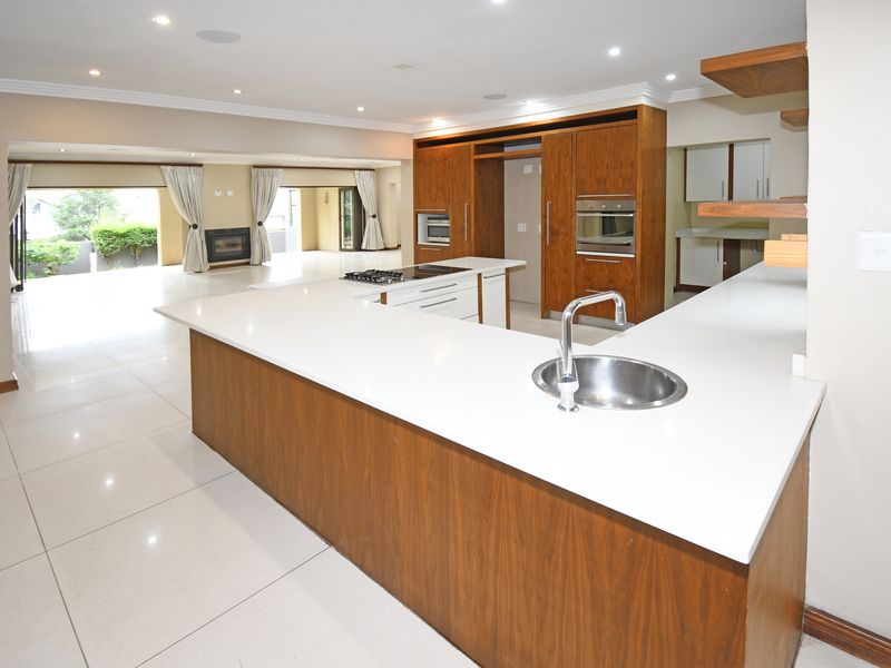 Spacious open-plan kitchen featuring a large island with a sink, built-in oven, gas hob, and ample wooden cabinetry, flowing into the living area.