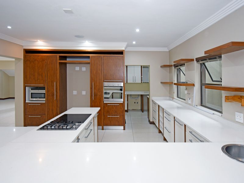 Modern kitchen featuring wood-veneer cabinetry, white stone countertops, a central island with a gas hob, built-in oven, and an adjacent scullery area.