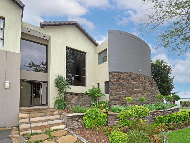 Modern architectural front facade featuring a striking curved wall with natural stone cladding, large glass windows, and a landscaped garden entrance.