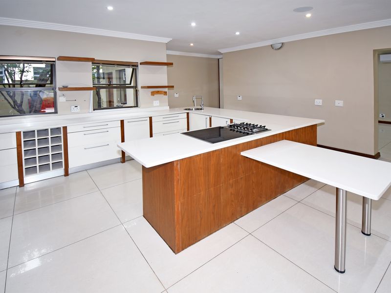 Modern open-plan kitchen featuring white cabinetry, stone countertops, a central island with a built-in gas hob, and tiled flooring throughout.
