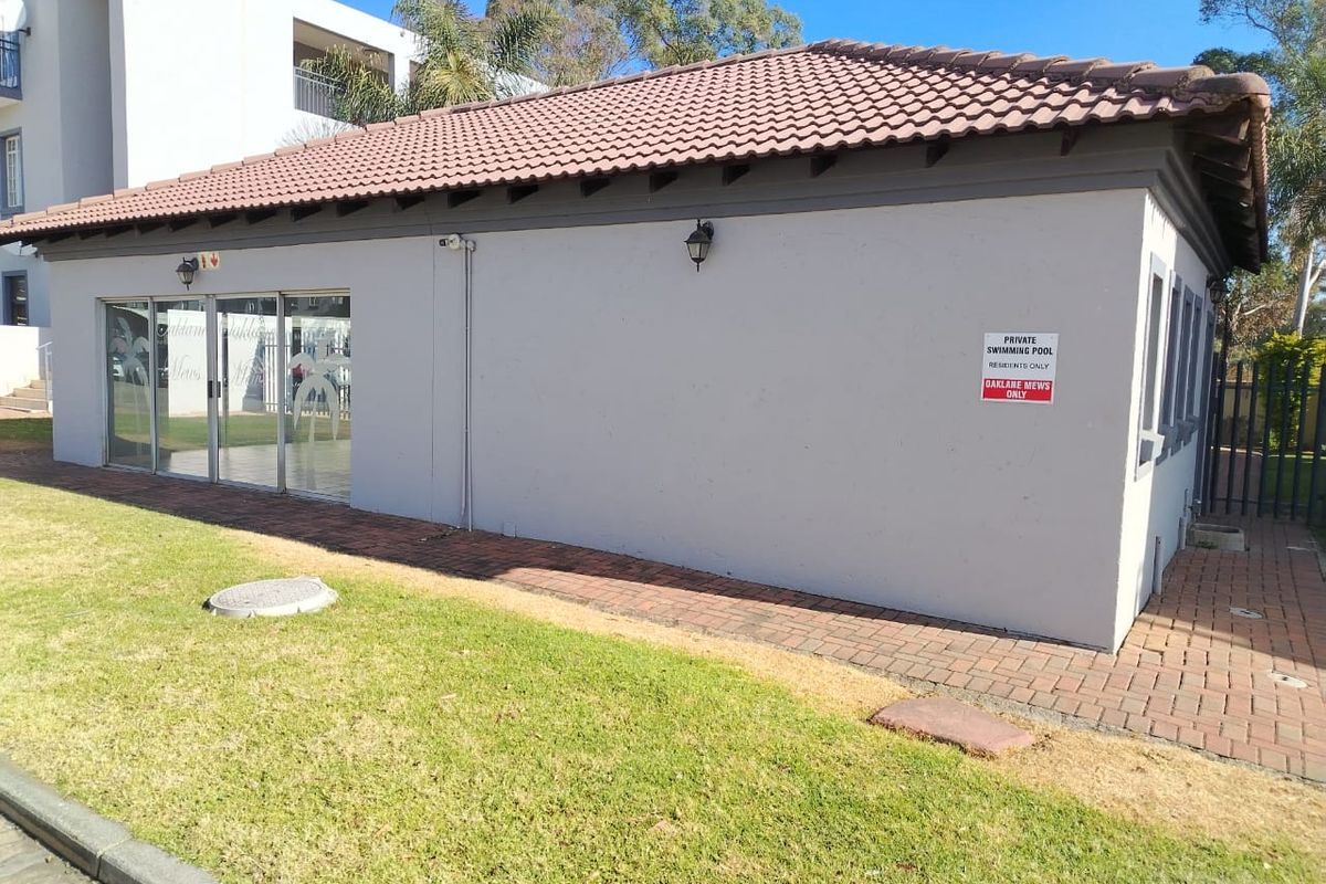 Exterior view of a communal building featuring a tiled roof, paved walkway, and glass sliding doors, situated within a residential apartment complex.