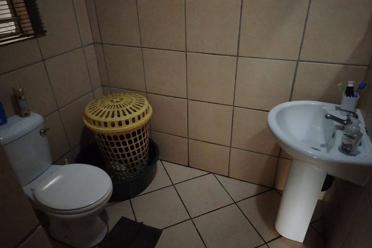A functional bathroom featuring a pedestal sink, standard toilet, and tiled walls and flooring.