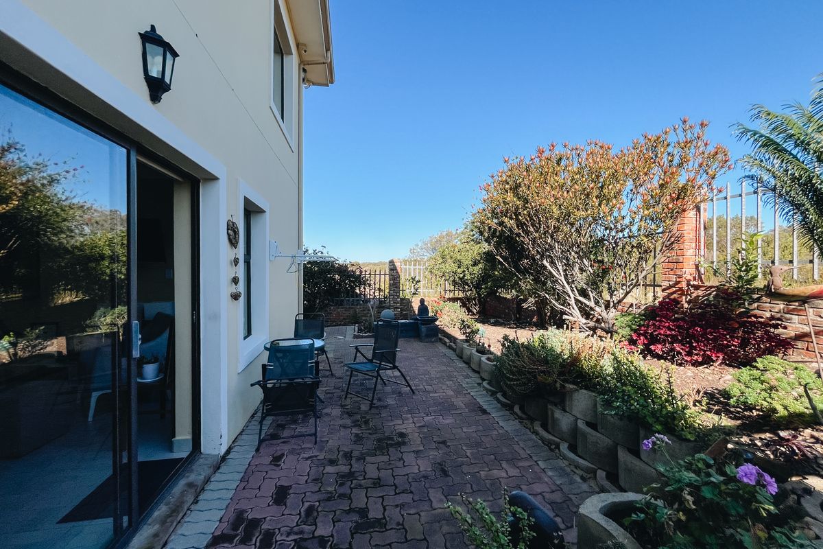 A rear patio area featuring paved flooring, sliding glass door access, and a landscaped garden border with established shrubs and brick boundary walling.