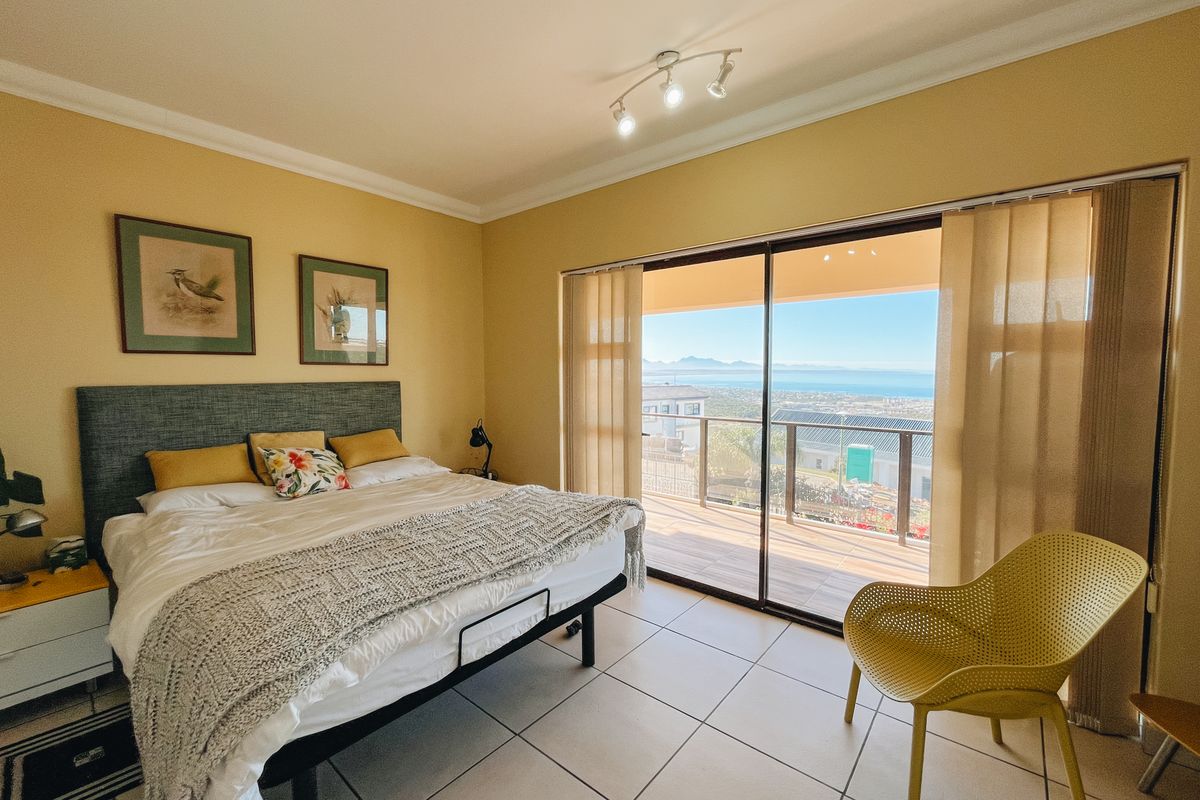 A bright bedroom featuring tiled flooring, a ceiling-mounted light fixture, and large sliding glass doors that open onto a balcony with scenic coastal views.