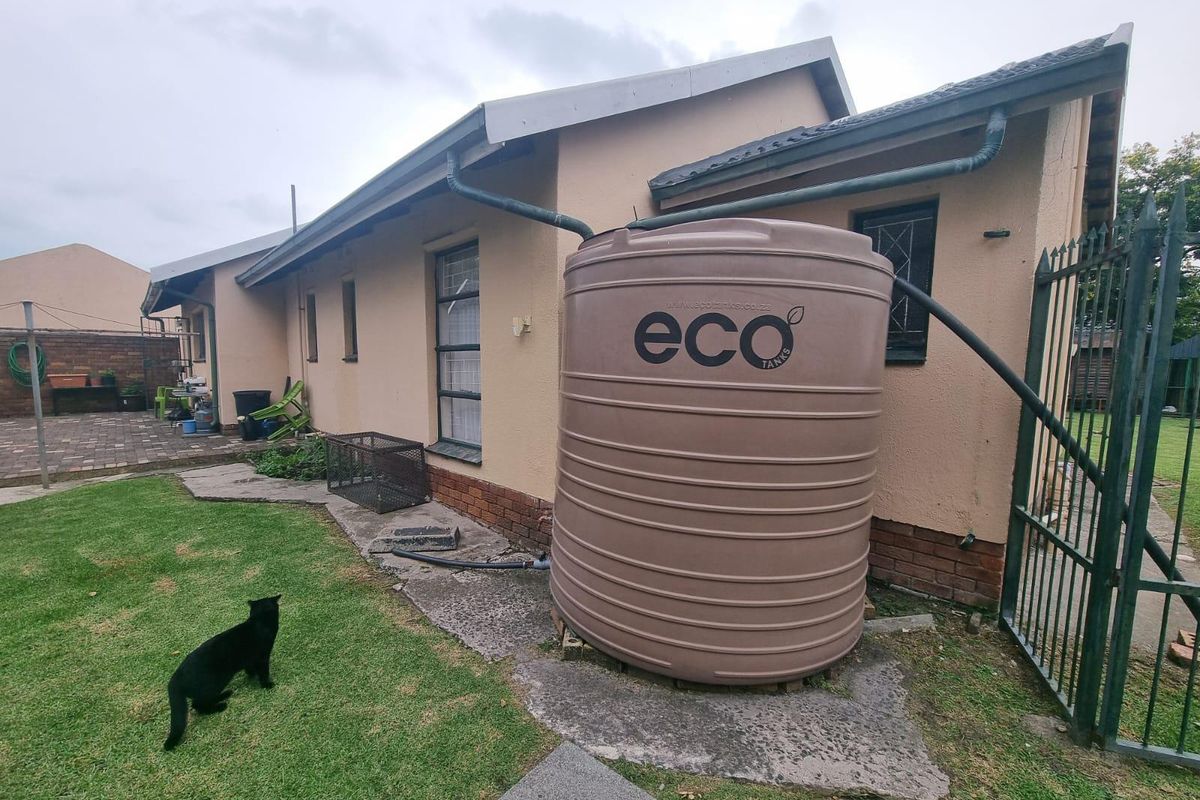 Rear exterior view of the property featuring a large water storage tank, gutter system, and paved patio area adjacent to the garden.