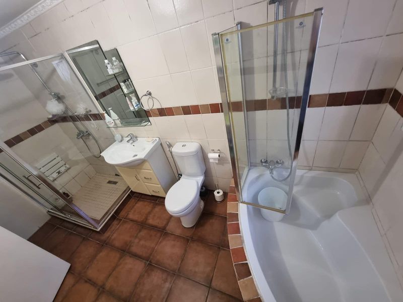 A functional bathroom featuring a corner bathtub, separate glass-enclosed shower, pedestal vanity, and toilet with tiled walls and flooring.