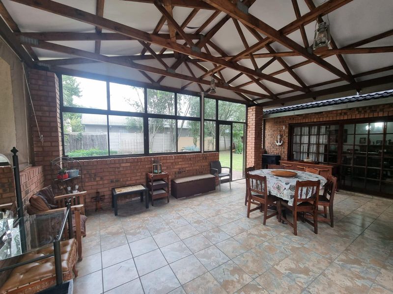 Spacious enclosed patio featuring exposed timber roof trusses, brick walls, and large glass windows overlooking the rear garden.