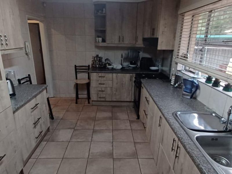 Functional kitchen featuring light wood-grain cabinetry, granite-look countertops, double stainless steel sink, and tiled flooring with ample storage space.