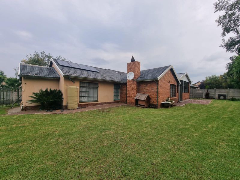 Rear view of the house featuring a brick and plaster facade, tiled roof, solar panels, water tank, and a spacious lawn.