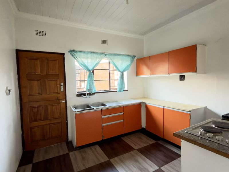 A functional kitchen featuring original cabinetry, a double sink, and a built-in hob, offering potential for a modern renovation.