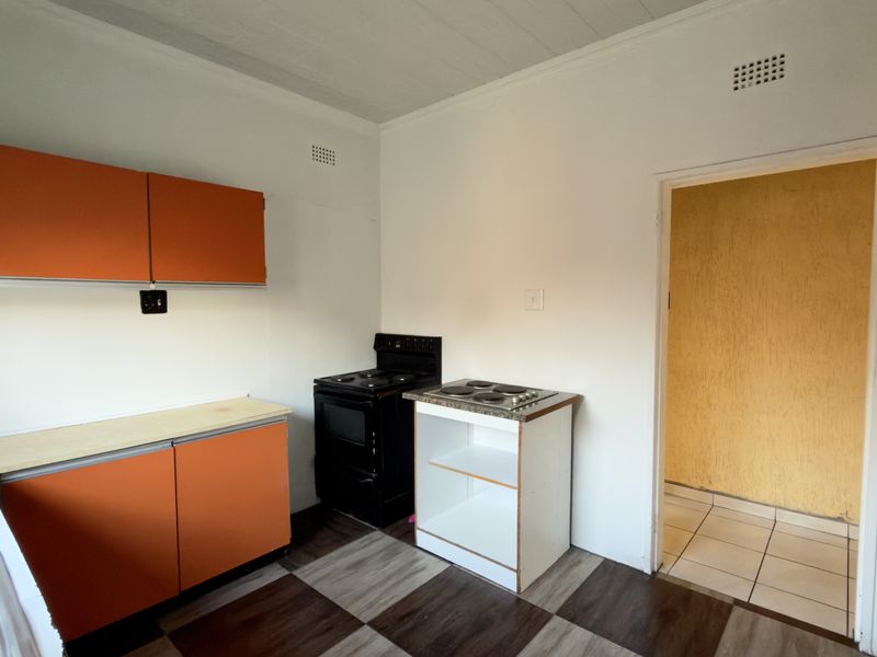 A functional kitchen space featuring orange cabinetry, a stainless steel sink, and a freestanding stove, offering potential for modernization and layout optimization.