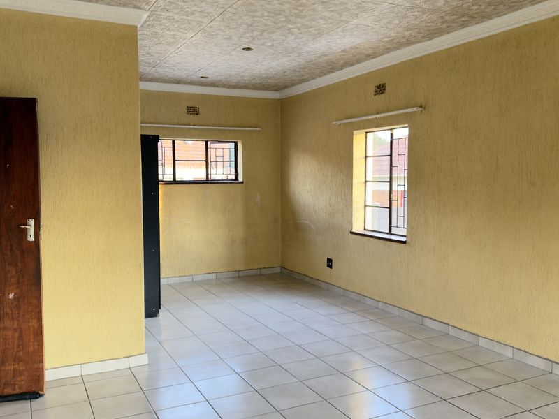 An empty living area featuring tiled flooring, textured yellow walls, and coved ceilings, offering a blank canvas for renovation and interior design updates.