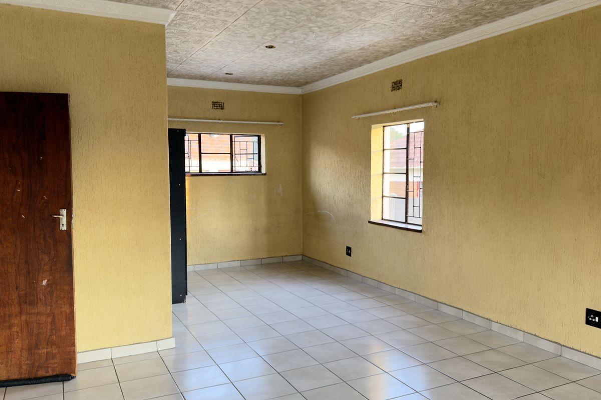 An empty living area featuring tiled flooring, textured yellow walls, and coved ceilings, offering a blank canvas for renovation and interior design updates.