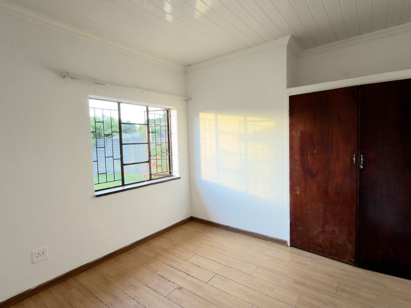 A bright, empty bedroom featuring laminate flooring, a built-in wooden wardrobe, and a window with security bars.