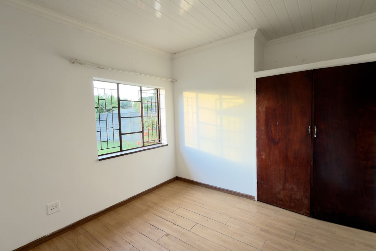 A bright, empty bedroom featuring laminate flooring, a built-in wooden wardrobe, and a window with security bars.