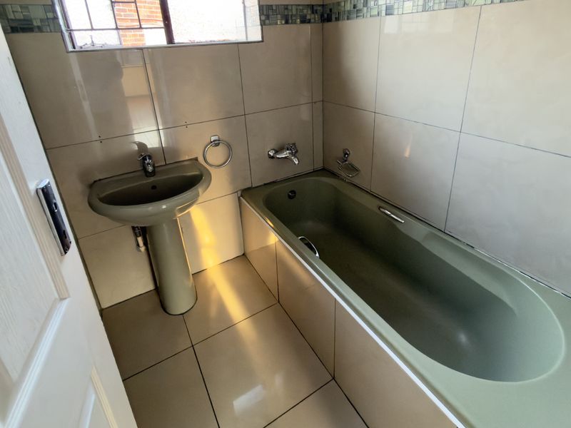 A functional bathroom featuring tiled walls and flooring, equipped with a pedestal basin and a bathtub with chrome fixtures.