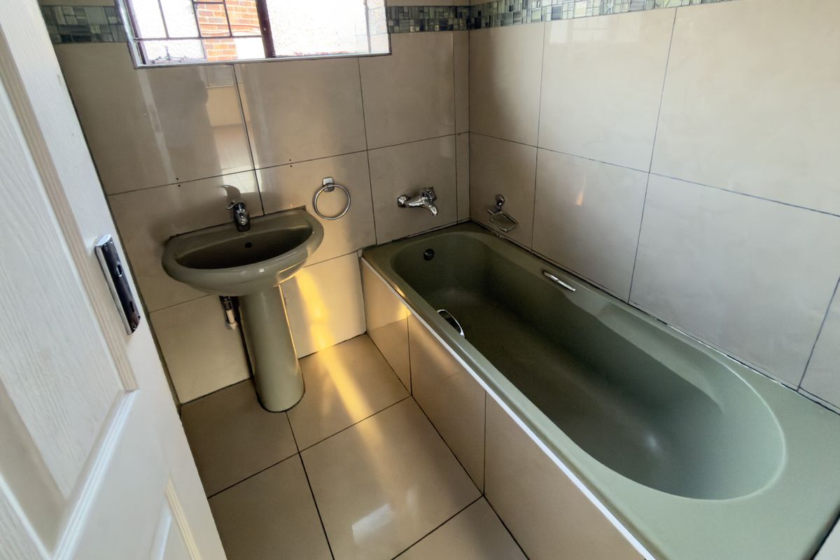 A functional bathroom featuring tiled walls and flooring, equipped with a pedestal basin and a bathtub with chrome fixtures.